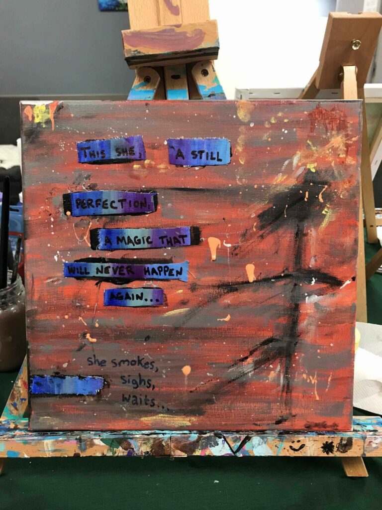 A painted canvas on an easel shows a quote with words collaged in blue and purple rectangles: “This she a still perfection a magic that will never happen again… she smokes, sighs, waits.” The background is abstract in brown and orange.