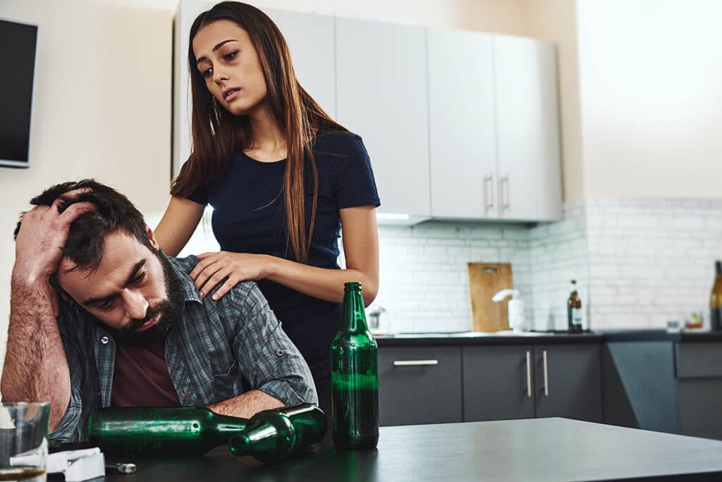 woman standing by man drinking wondering how to help an alcoholic