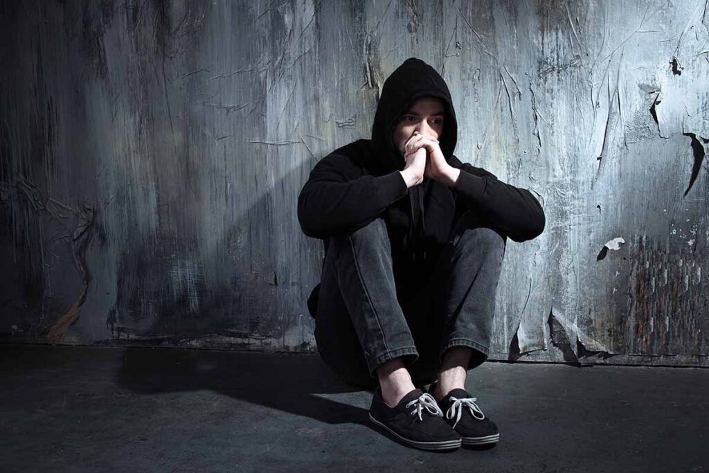 is addiction a disease figure in black hoodie sitting against grey wall