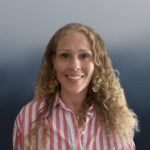 A woman with long curly blonde hair smiles at the camera, wearing a pink and white striped shirt, with a gradient blue background behind her.